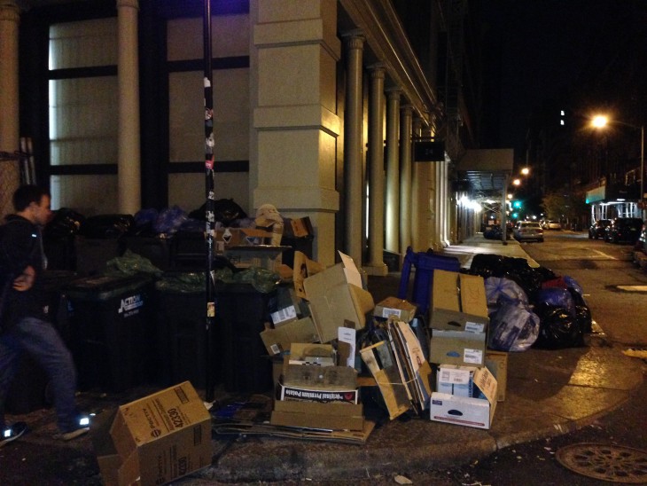 A pile of garbage on the curb of a street at night in New York City.