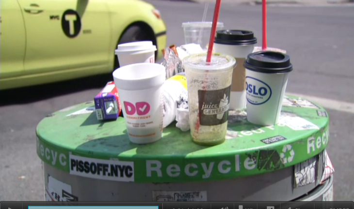 Empty plastic and styrofoam cups and bottles sitting on top of a green-toped recycling canister as a yellow-green taxi goes by.